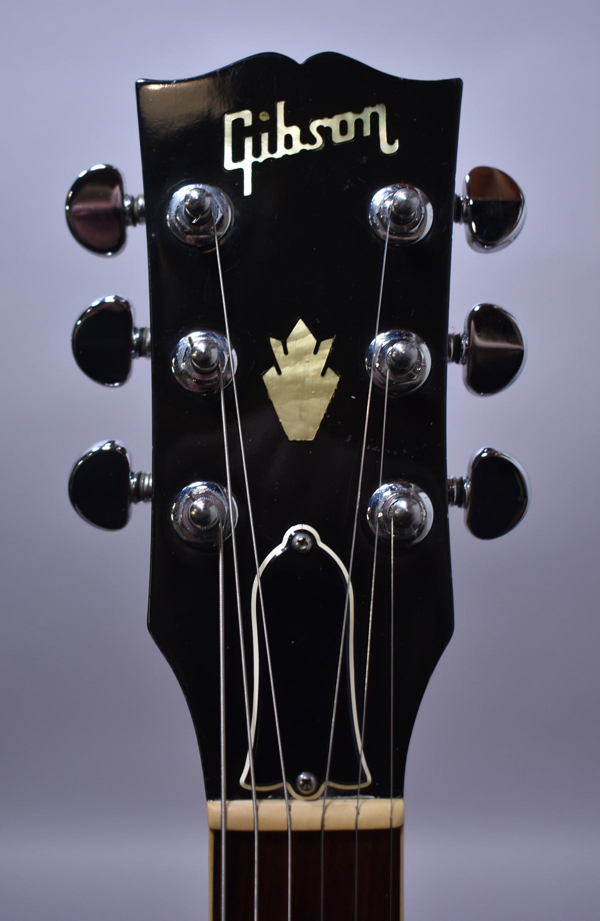 The guitar's black headstock with a gold crown inlay and chrome tuners is shown from the front, with light surface scratches.