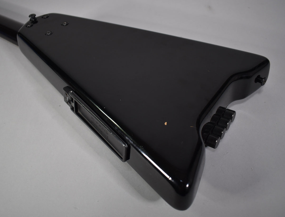 The black bass guitar's body is angled, showing its glossy finish, four black control knobs, and a rectangular side input jack.