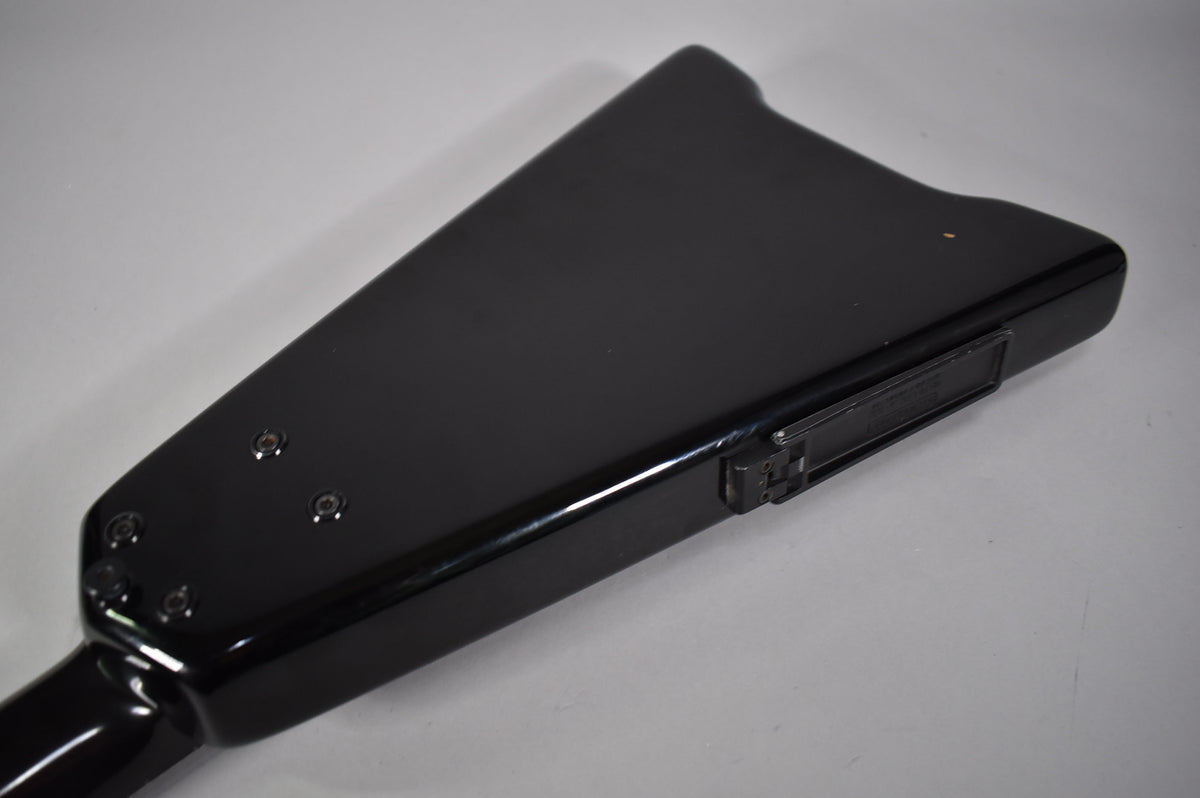 Close-up of the bass guitar's glossy black body, showing the neck joint with four visible screws and a small rectangular control plate.