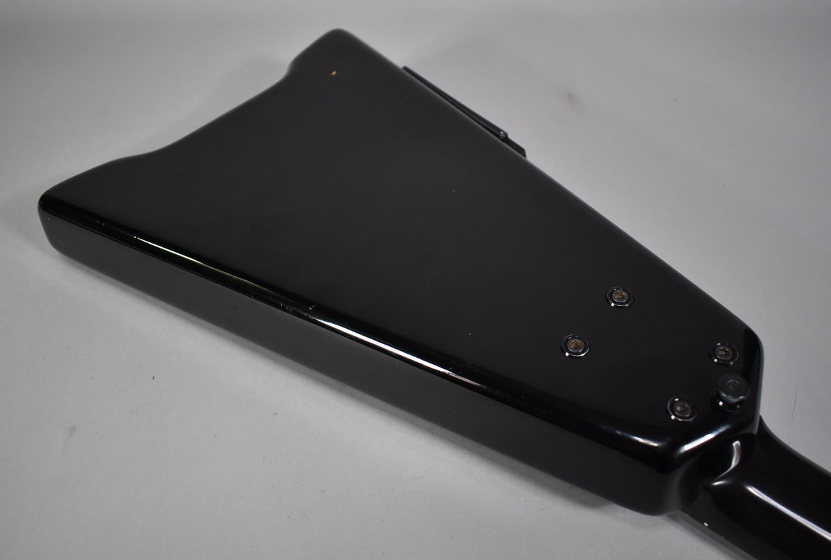The back of the black bass body is shown from an angle, with four visible neck bolts and a small ding near the top edge.
