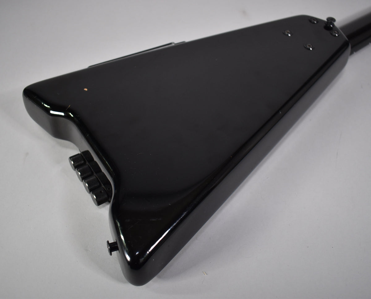 Rear view of the black Steinberger bass body, showing the glossy finish, four black bridge saddles, and a small chip on the lower bout.