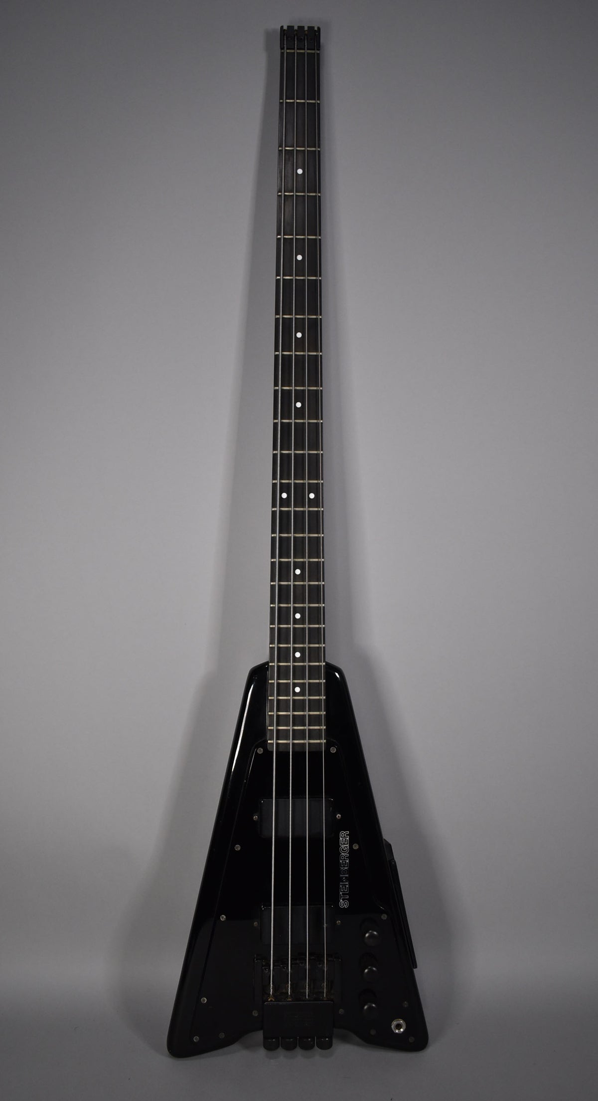 Full-length, head-on view of a black V-shaped bass with a glossy finish, four strings, and a dark fretboard with white dot inlays.