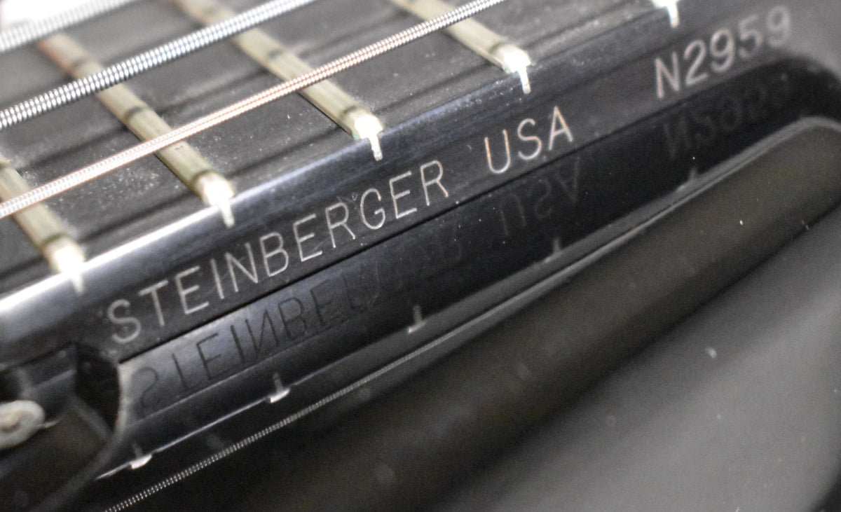 Close-up of the black bass's fretboard and strings, showing light dust and reflections on the glossy finish.