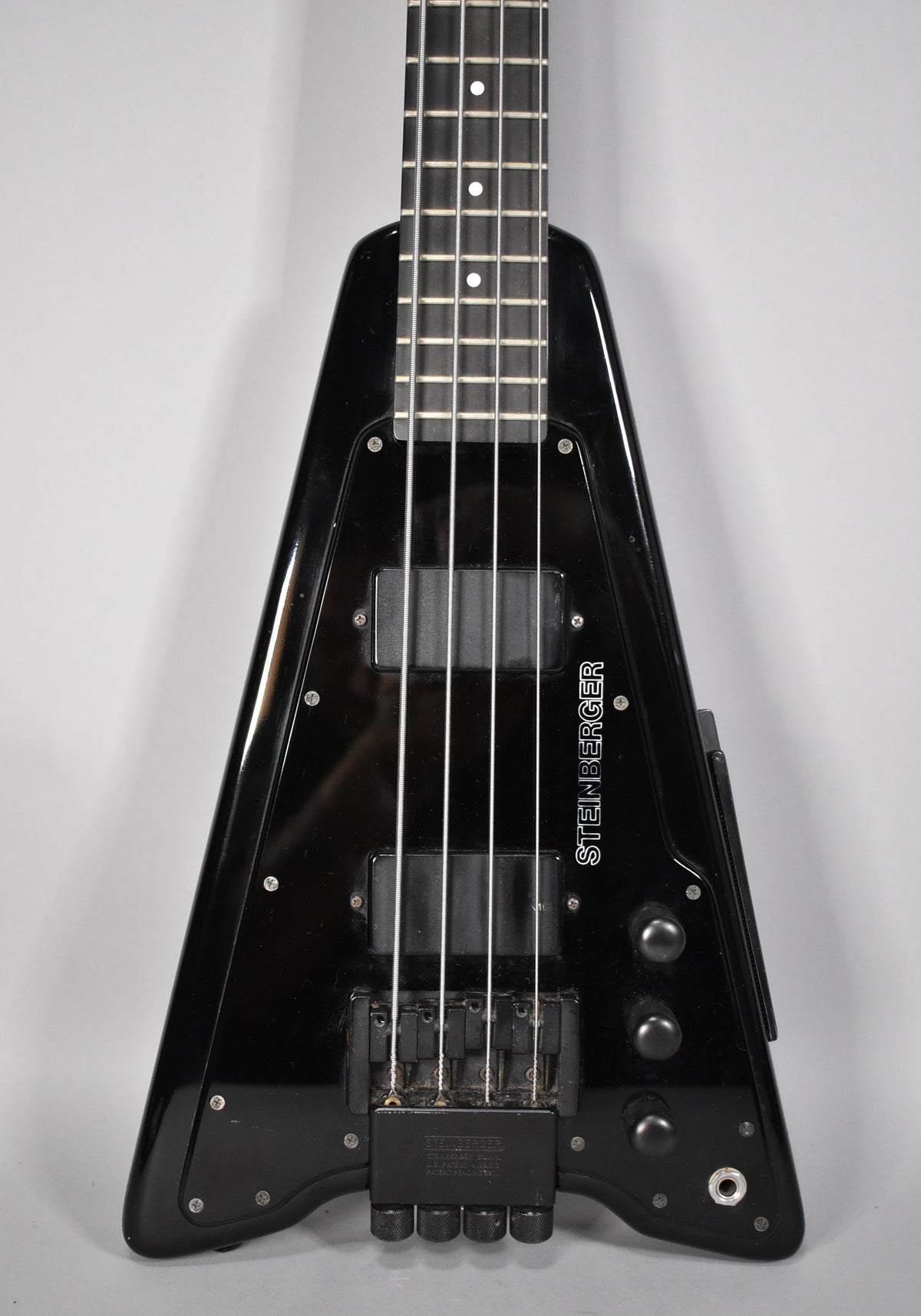 Full-frame view of the glossy black bass, showing the fretboard, two pickups, bridge, four tuning knobs, and input jack.