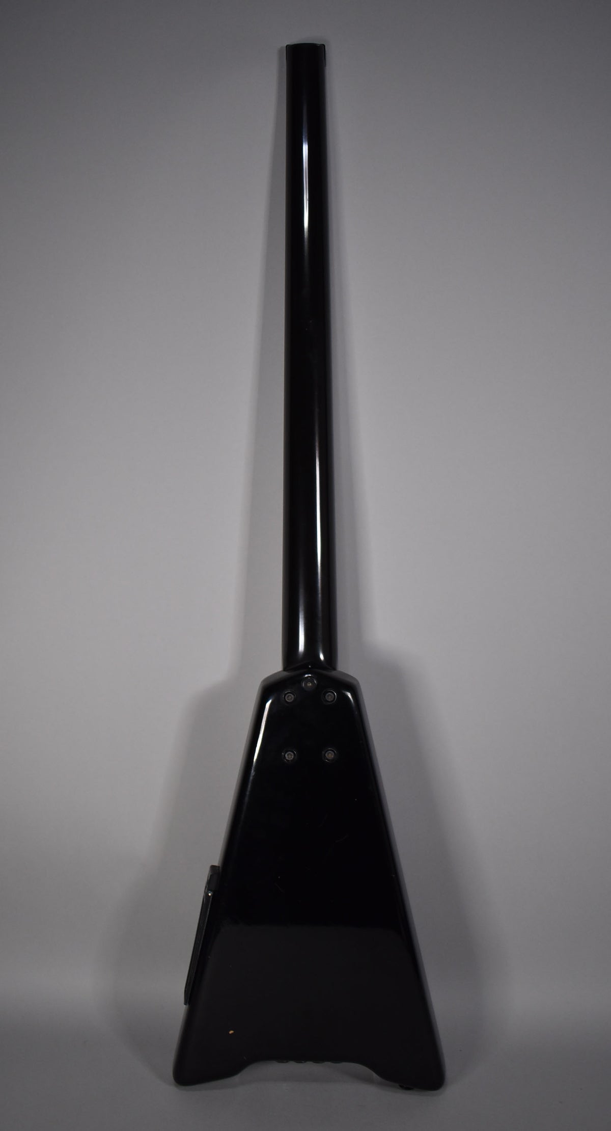 The black bass guitar is shown from the back, neck extending upwards from the triangular body, with four visible neck bolts.