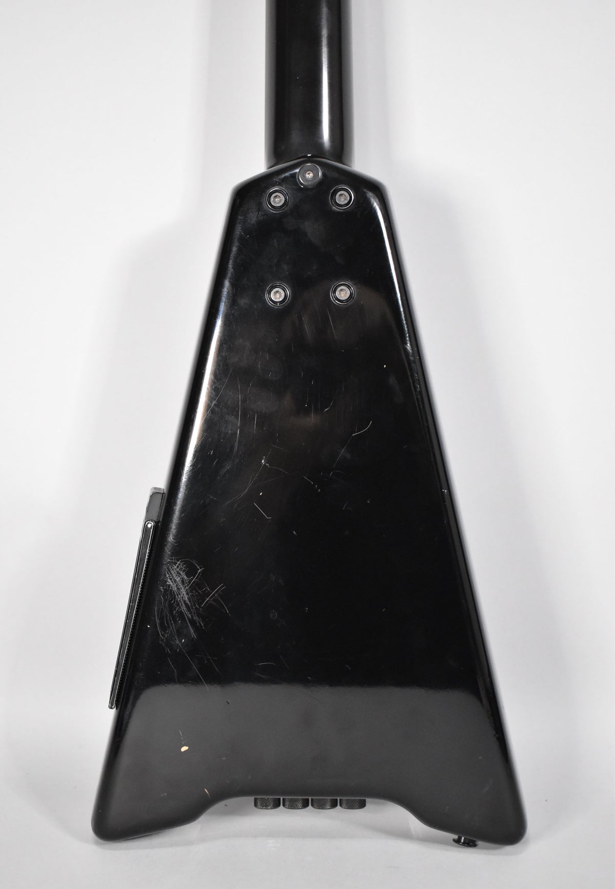 The back of the black bass guitar body, showing the neck joint, four control knobs, and many surface scratches.