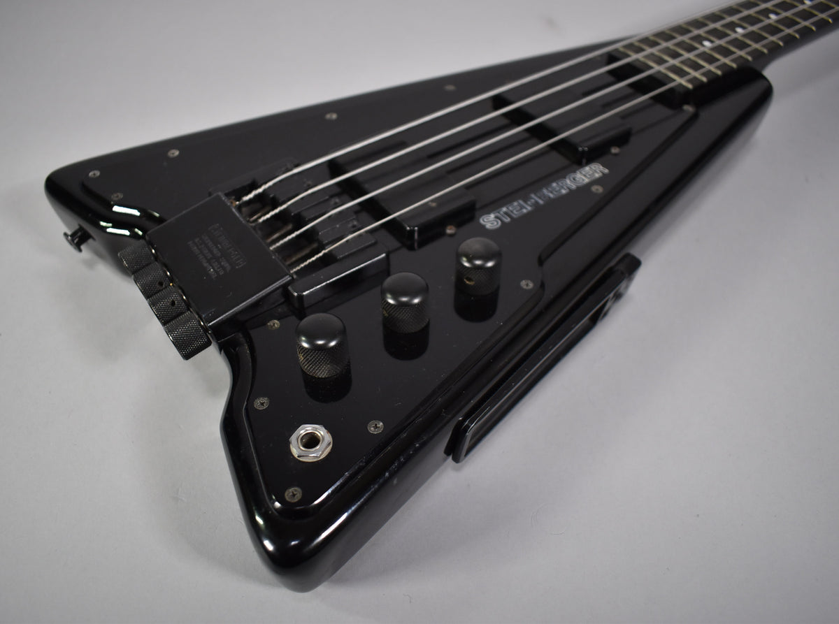 Close-up of the black V-shaped body, showing three knurled control knobs, the output jack, and the bridge with fine tuners.