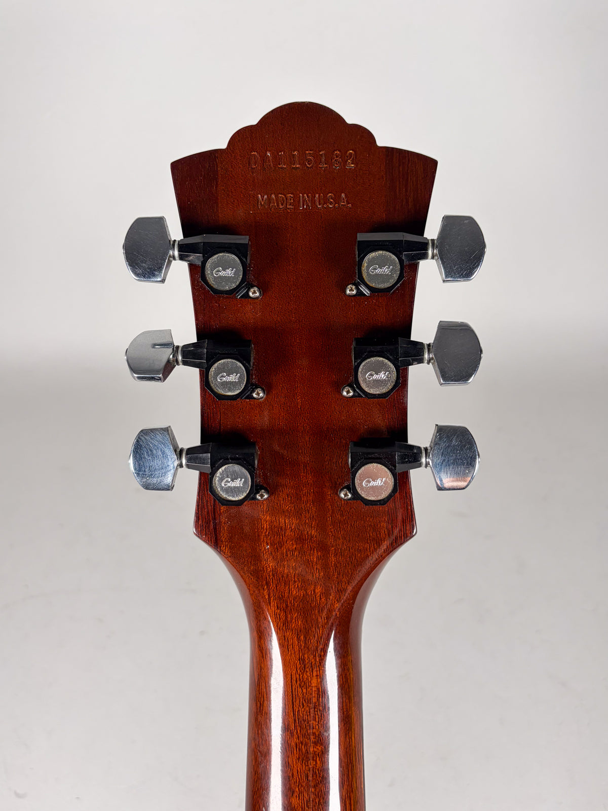 The guitar's mahogany headstock and neck are shown from behind, with six chrome tuners and black tuner buttons.