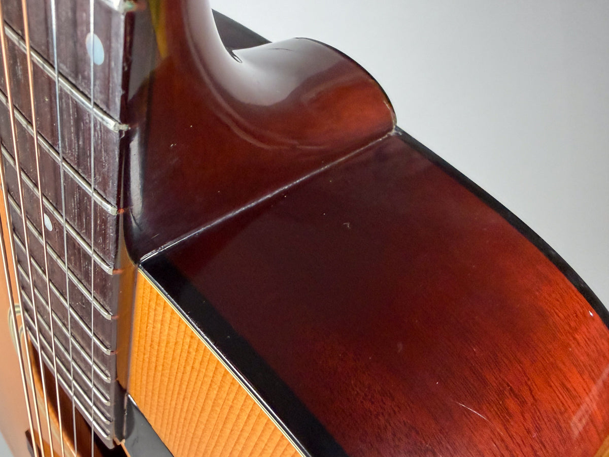Close-up of the guitar's neck heel and upper bout, showing dark brown wood with light scratches and a small chip on the heel.