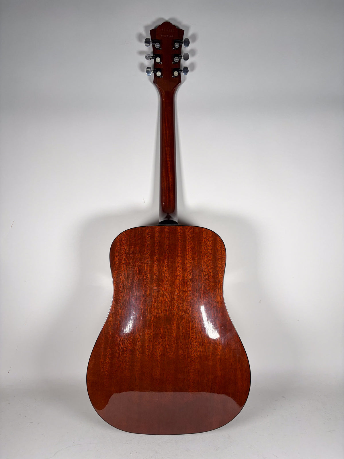 The guitar's glossy reddish-brown back and neck are visible from behind, with six chrome tuners on the headstock.