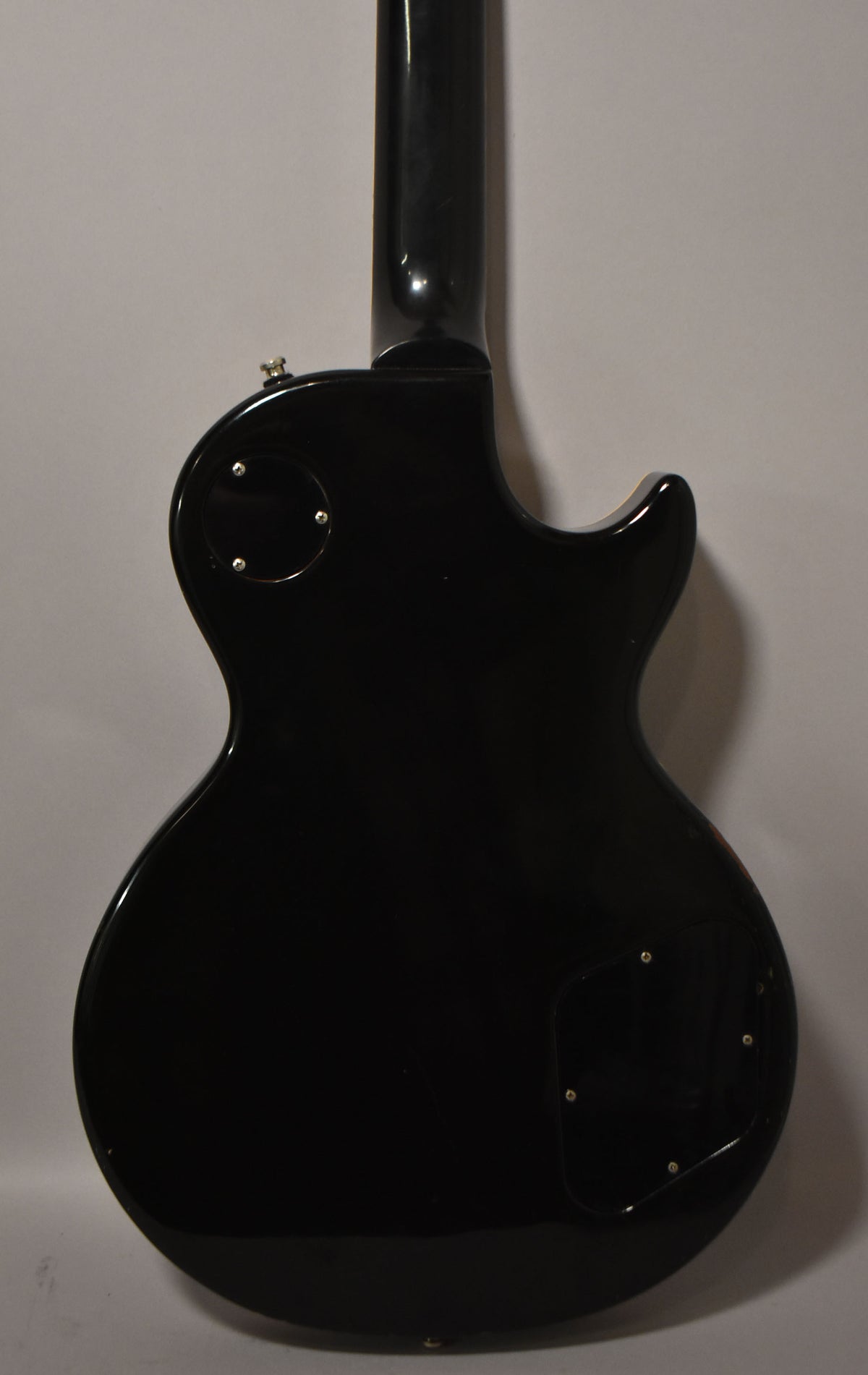 Full back view of the glossy black guitar, showing the neck joint, control cavity cover, and a circular access plate.