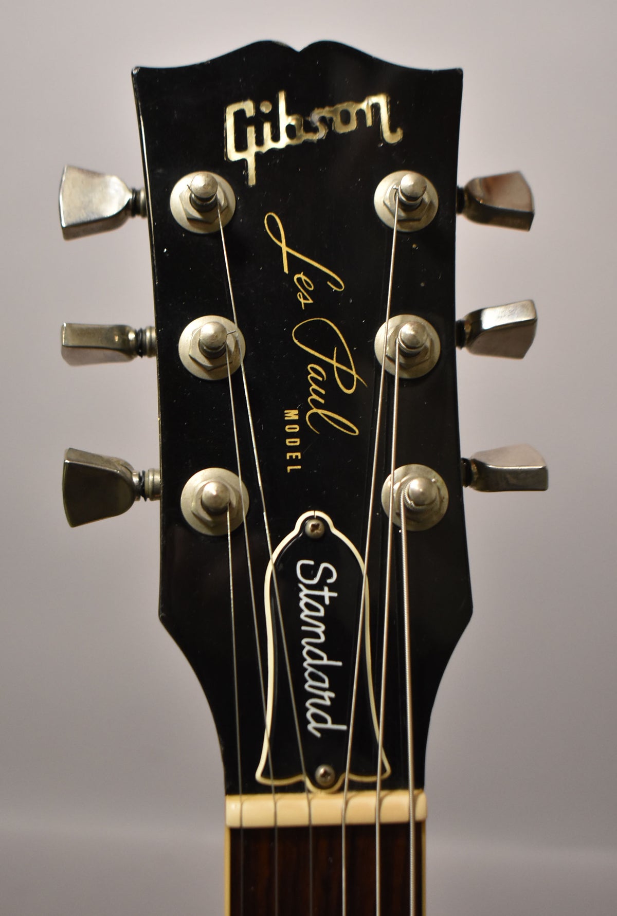 Close-up of the black headstock with gold lettering, showing six chrome tuners and a bell-shaped truss rod cover.