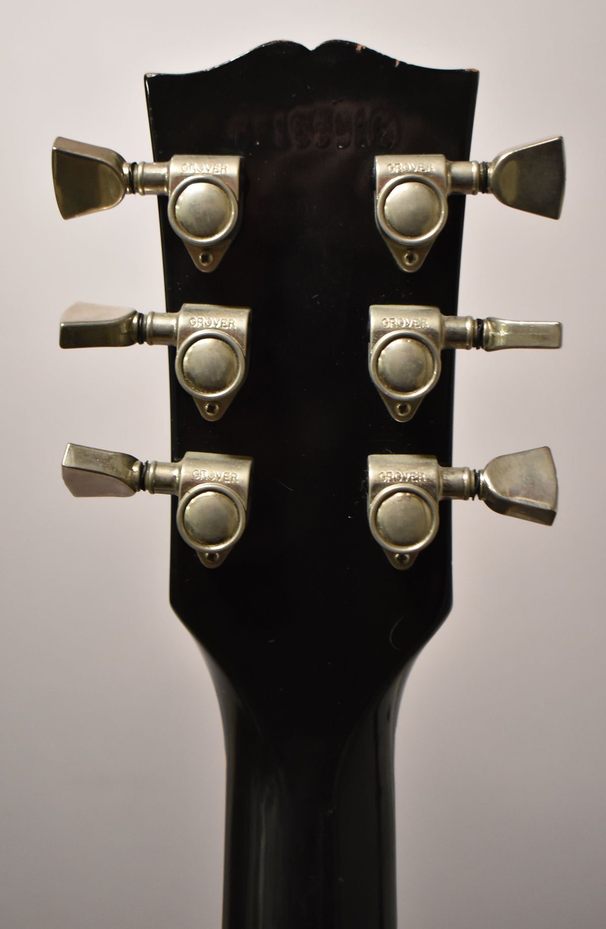 Rear view of the black headstock and neck, showing six worn silver tuners with trapezoid buttons and some finish wear on the top edge.