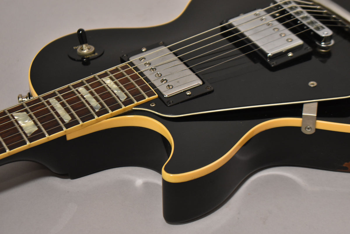 Close-up of the ebony Les Paul's upper body, showing the neck, cream binding, chrome humbuckers, and a worn strap button.
