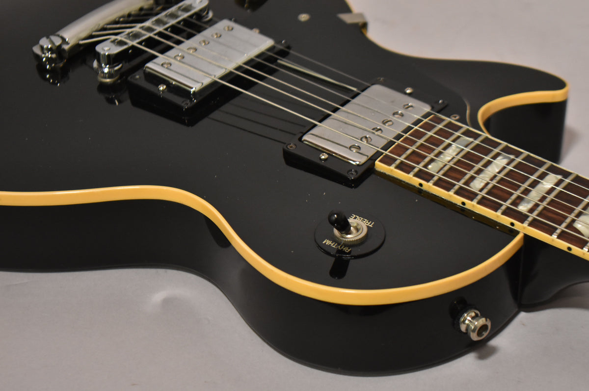 Close-up of the glossy black body, showing the chrome humbuckers, cream binding, and the "Rhythm/Treble" toggle switch.
