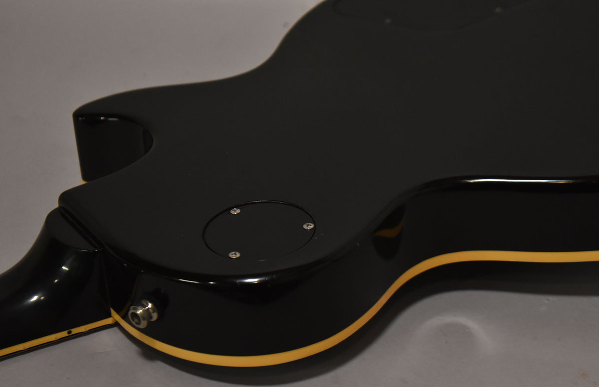 The lower bout of a glossy black guitar, showing the output jack, control cavity cover, and cream binding along the body edge.