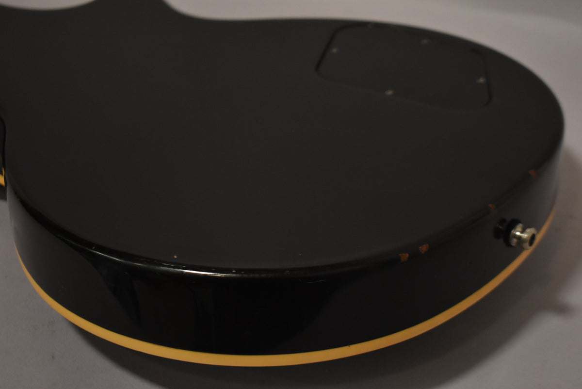 Close-up of the guitar's glossy black back and lower bout, showing cream binding, output jack, and several chips in the finish.