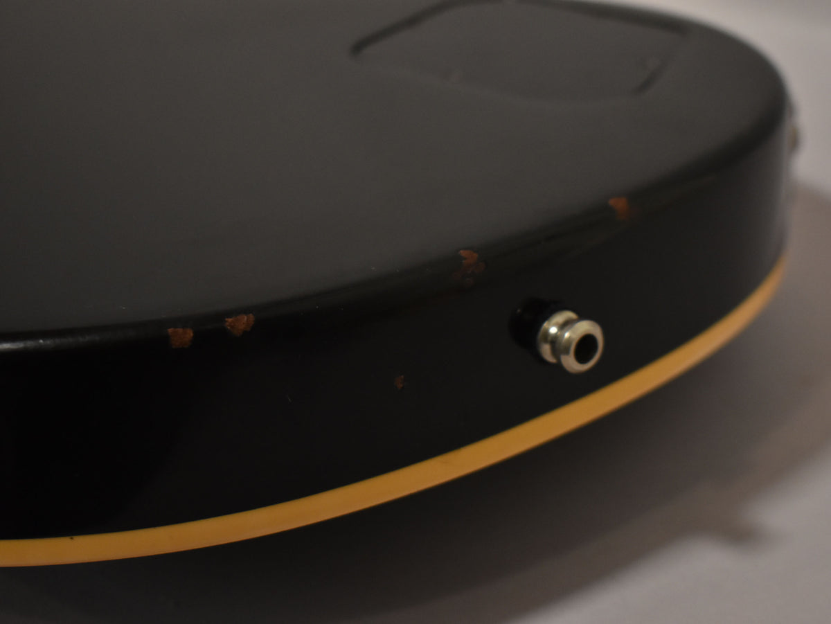 Close-up of the guitar's lower bout, showing the black finish, cream binding, and input jack, with several chips in the finish.