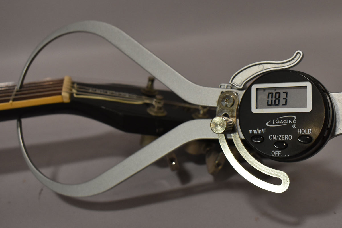 A digital caliper measures the nut width of the ebony Les Paul's headstock, displaying "0.83" on its screen.