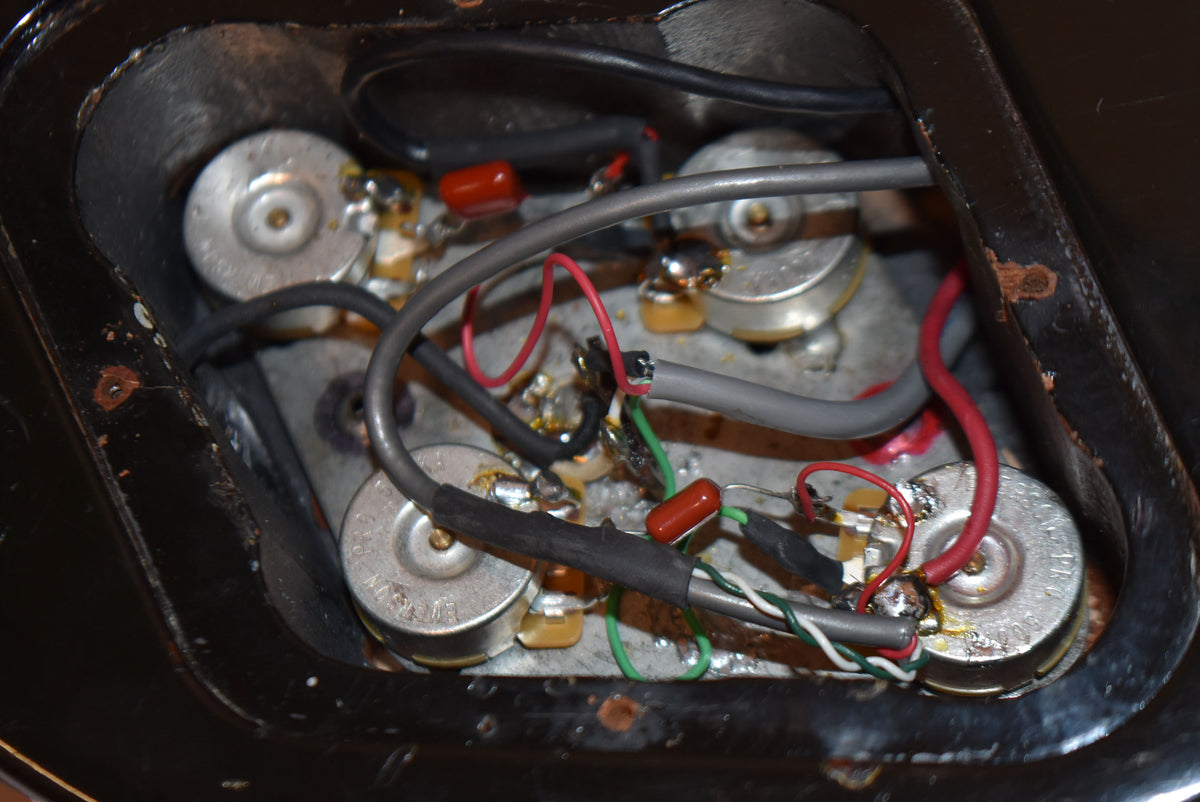 Close-up of the guitar's control cavity, revealing four silver potentiometers, orange capacitors, and various colored wiring.
