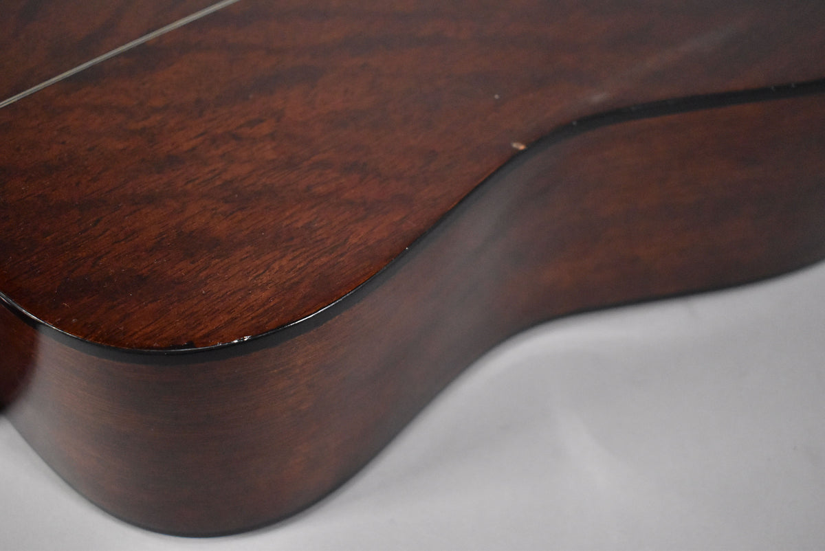 Close-up of the guitar's lower bout, showing the dark brown wood grain, gloss finish, and minor chips along the binding.