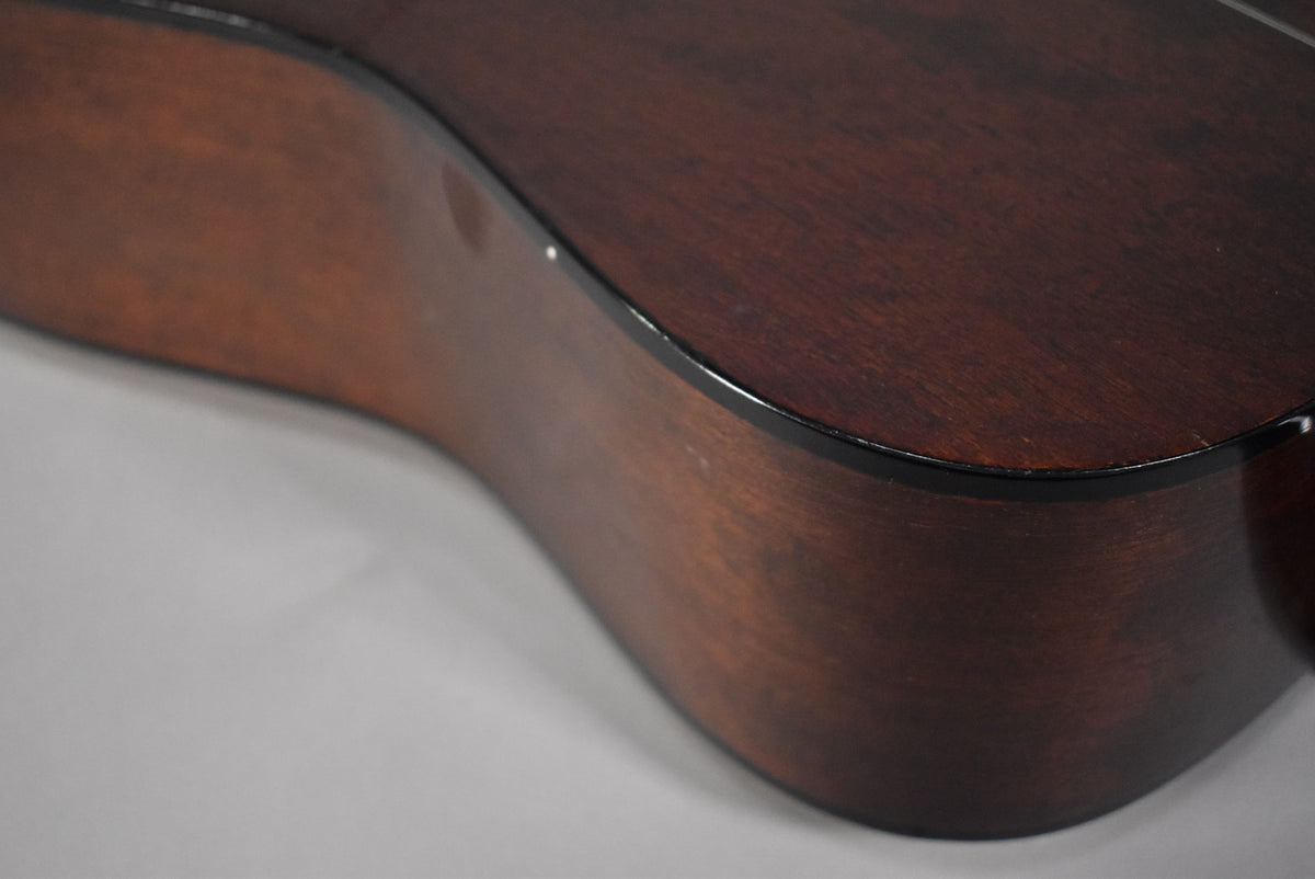The dark brown acoustic guitar body is angled, showing the side and part of the top with black binding and some minor scuffs.