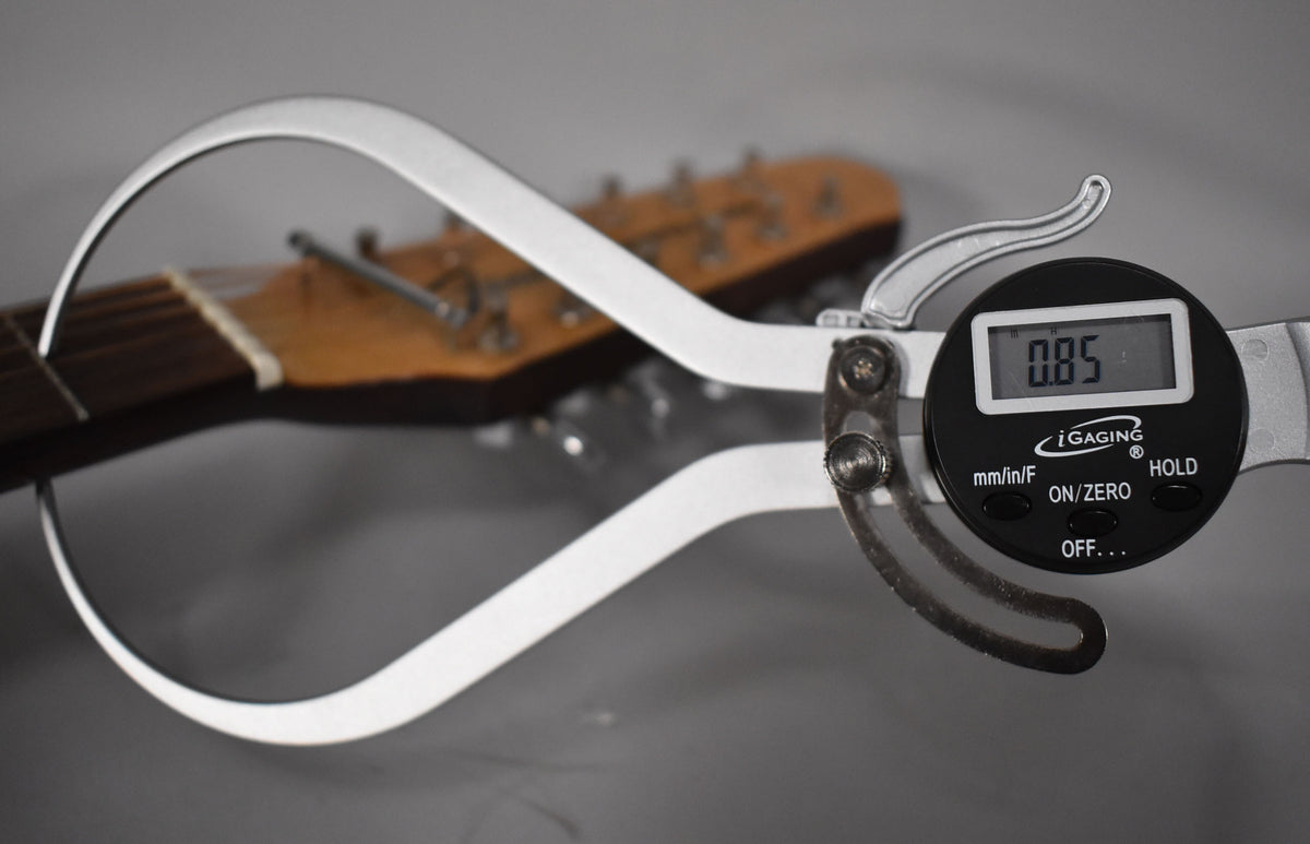 A digital caliper shows a reading of 0.85, measuring the nut of a guitar neck with a dark fretboard and light headstock.