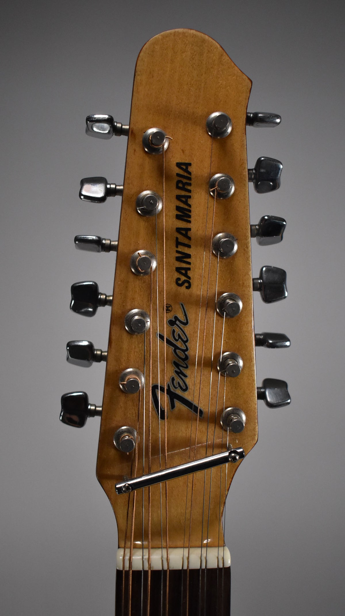 Close-up of the light brown headstock, showing 12 chrome tuners, a string tree, and light wear on the finish.