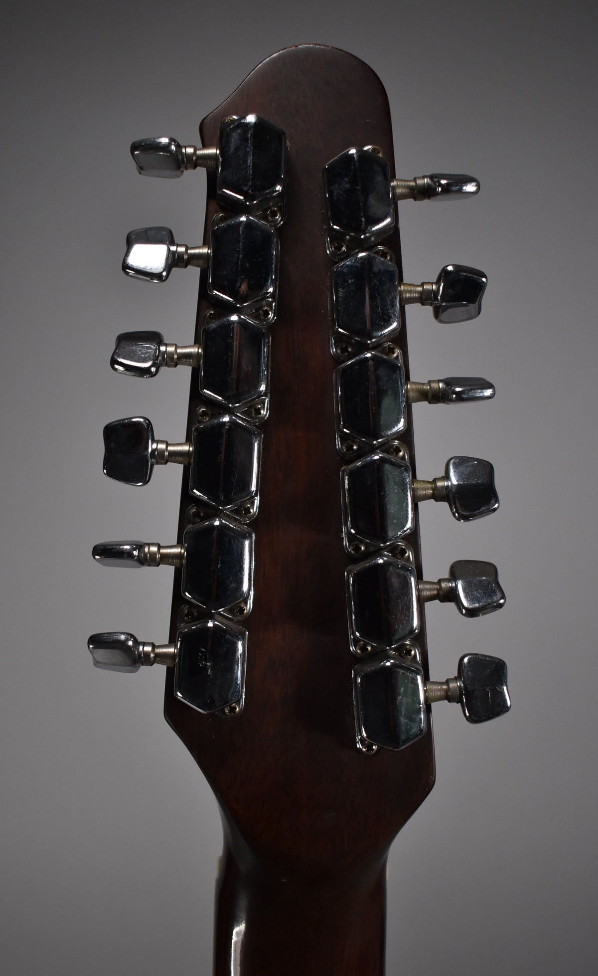 Rear view of the dark brown headstock, showing twelve chrome tuners with some tarnishing and light scratches.