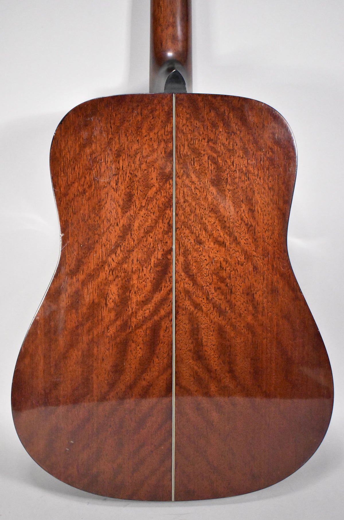The guitar's dark reddish-brown back, with a visible wood grain and center seam, shows minor scratches and dings.