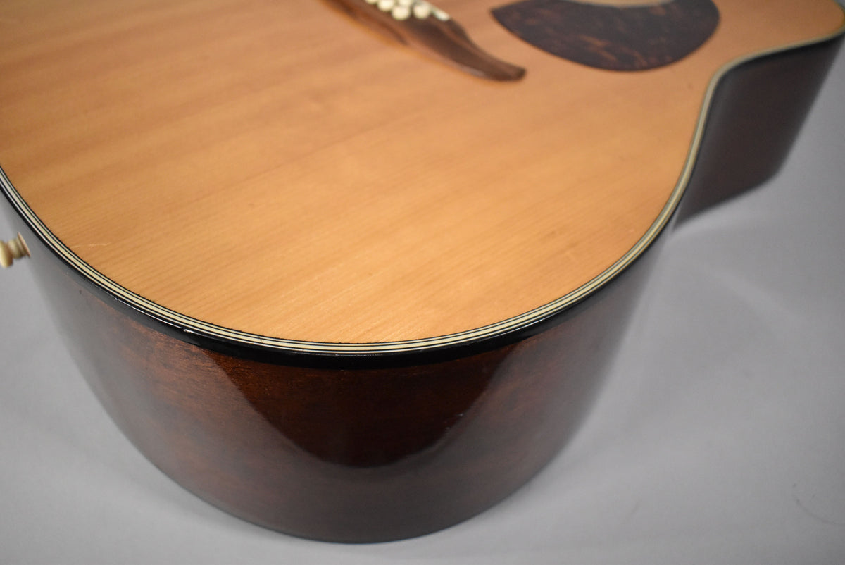 The lower bout of a 12-string acoustic guitar, showing the light wood top, dark wood sides, and multi-line binding.
