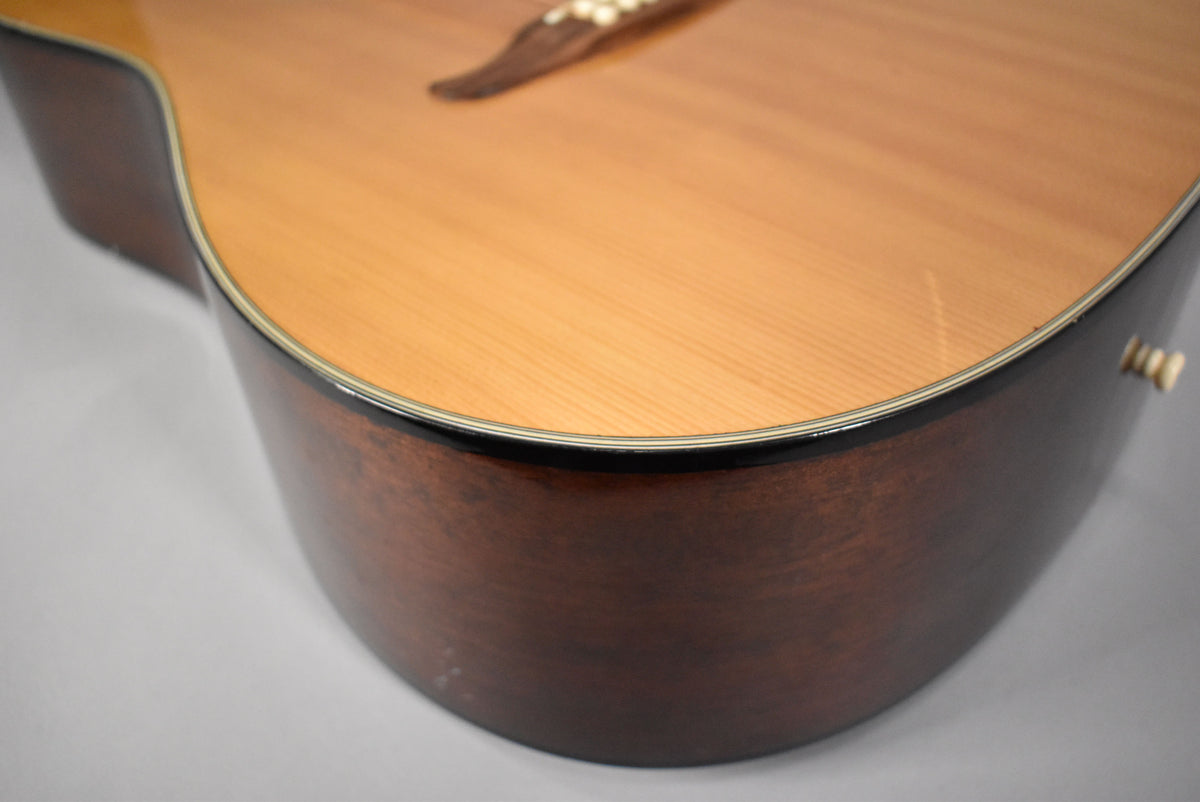 The lower bout of the acoustic guitar, showing a light wood top, dark brown sides, and a cream end pin.