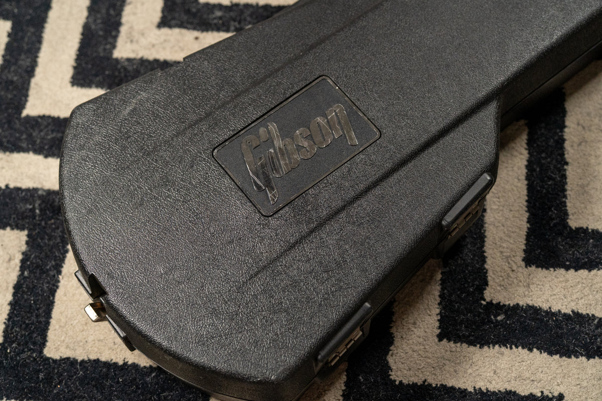 Overhead view of a black, textured hard case with a raised "Gibson" logo, showing minor scuffs and a silver latch.