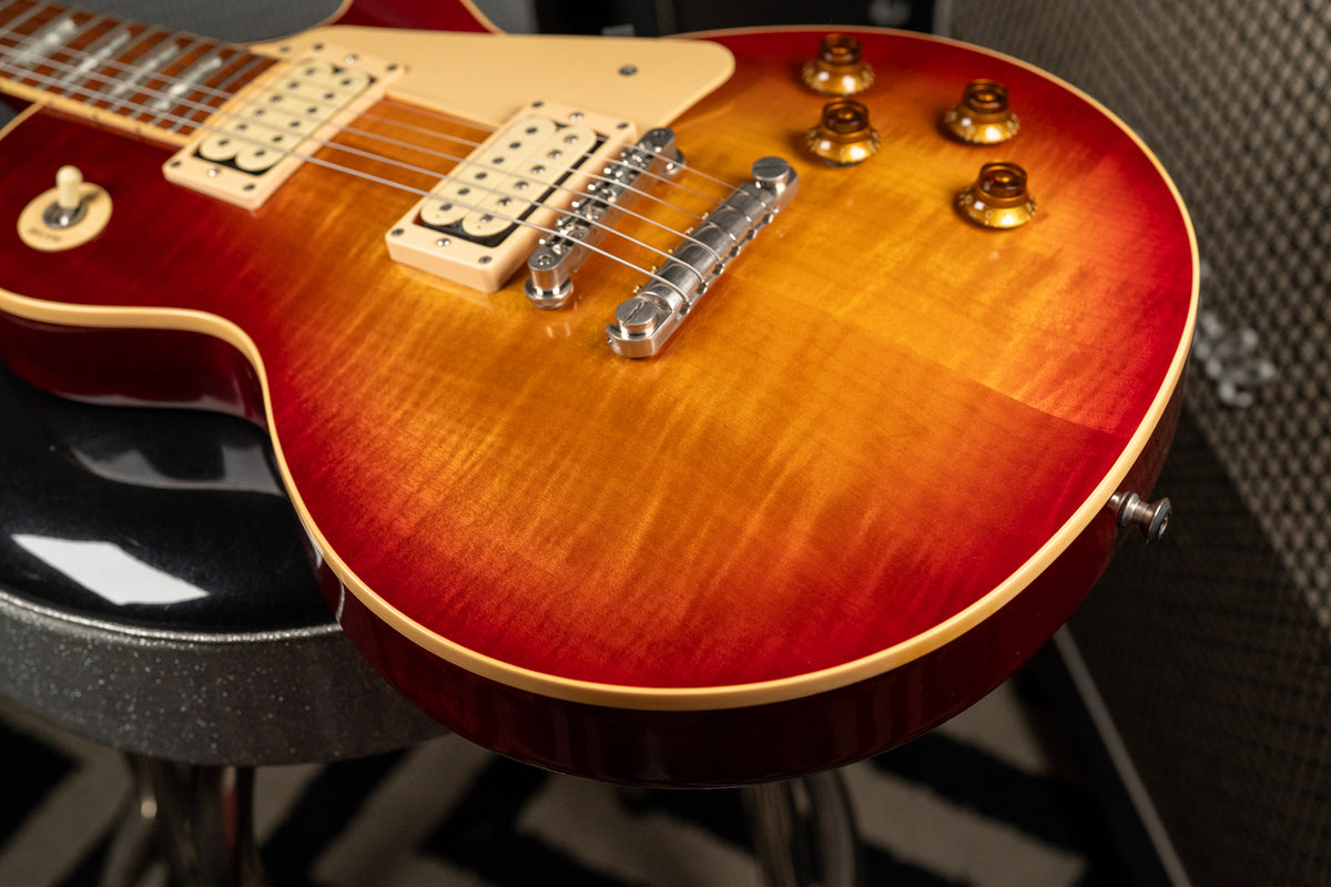 The guitar's cherry sunburst flame top is angled from the lower bout to the neck, showing cream pickups and gold top hat knobs.