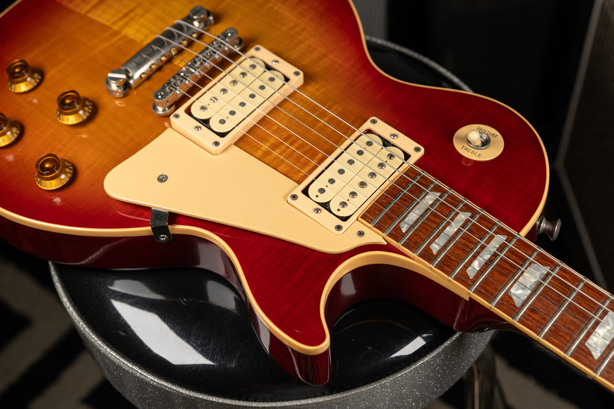 Close-up of a cherry sunburst guitar body, showing cream humbuckers, pickguard, gold top hat knobs, and trapezoid fretboard inlays.