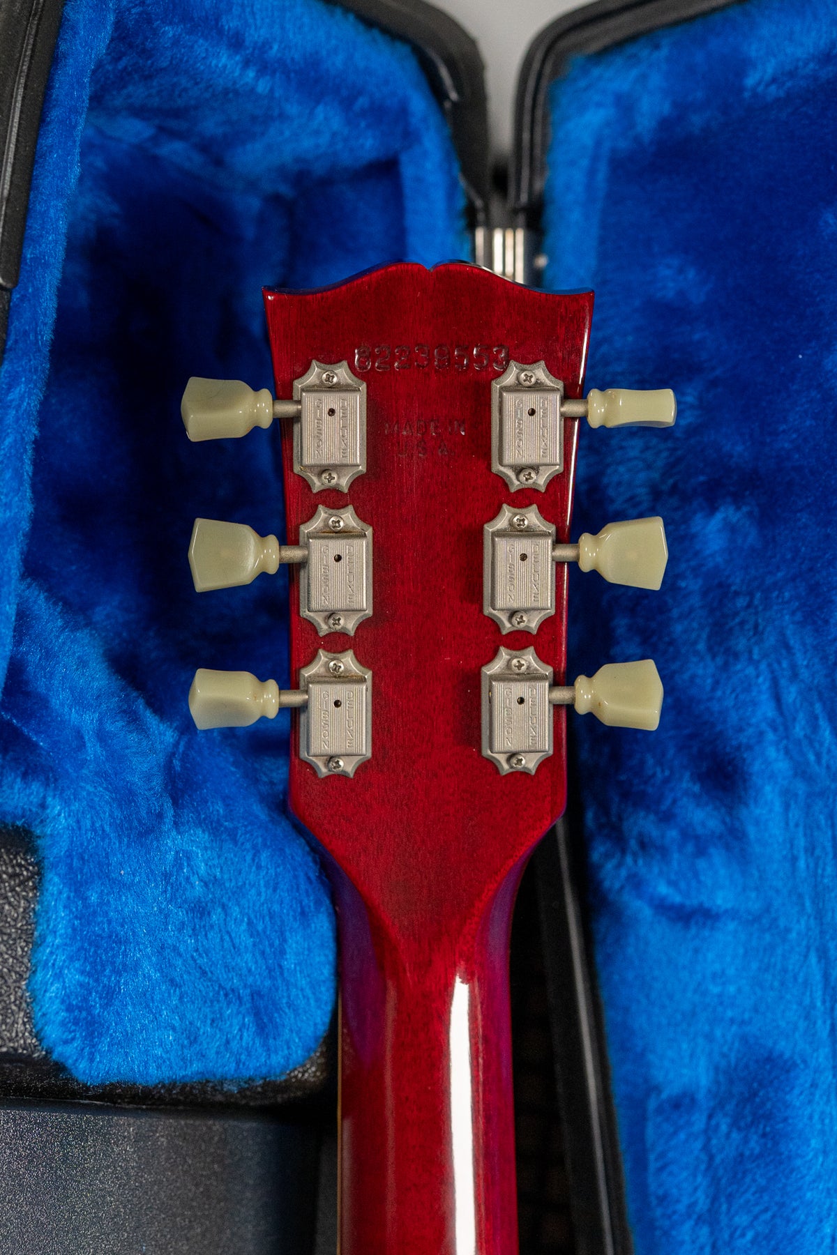 The back of the headstock and neck in cherry sunburst, with six cream-colored tuning pegs and chrome hardware, in a blue plush case.