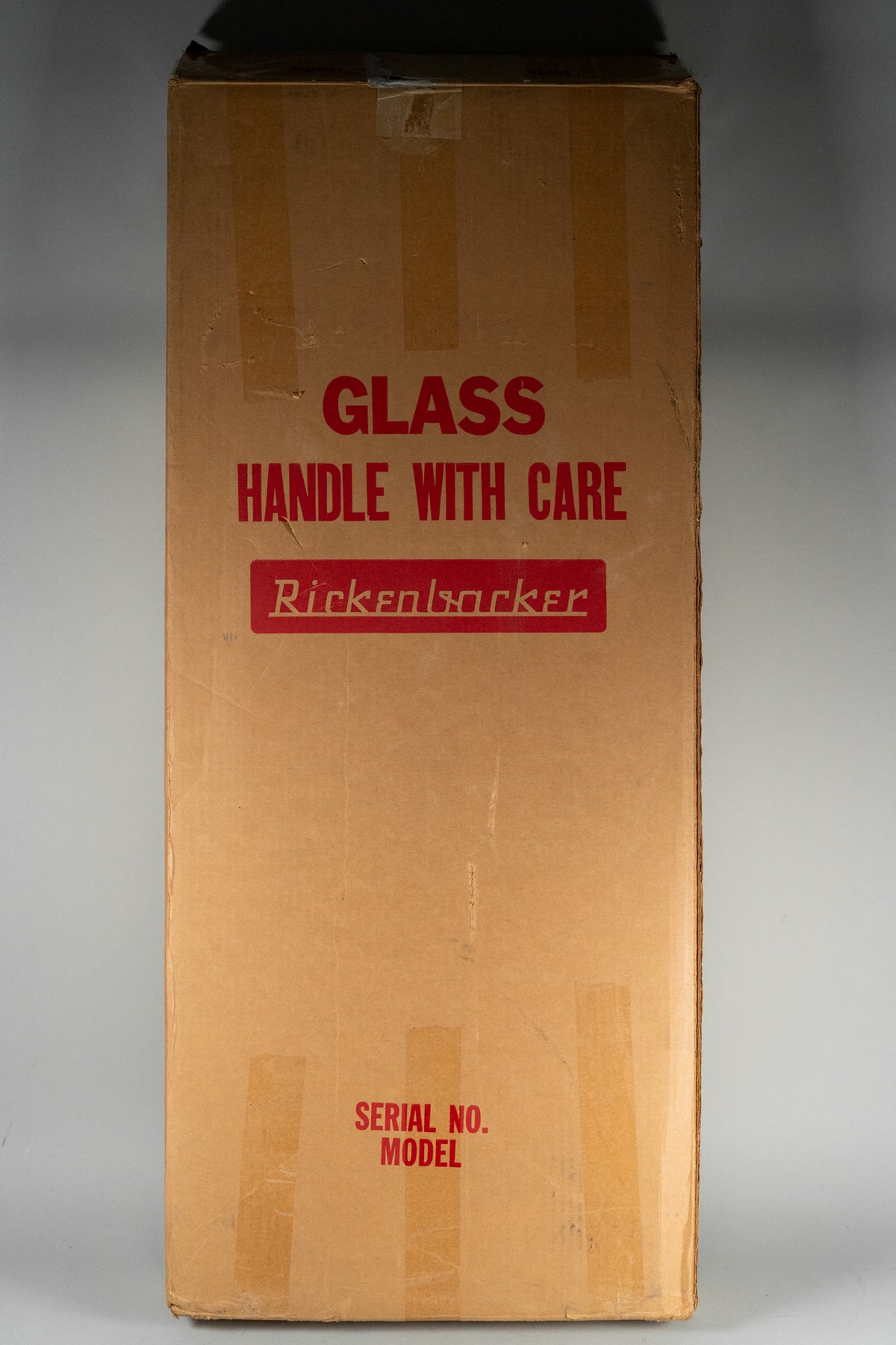The guitar's original shipping box, a tall brown cardboard carton with red "GLASS HANDLE WITH CARE" and "Rickenbacker" stencils.