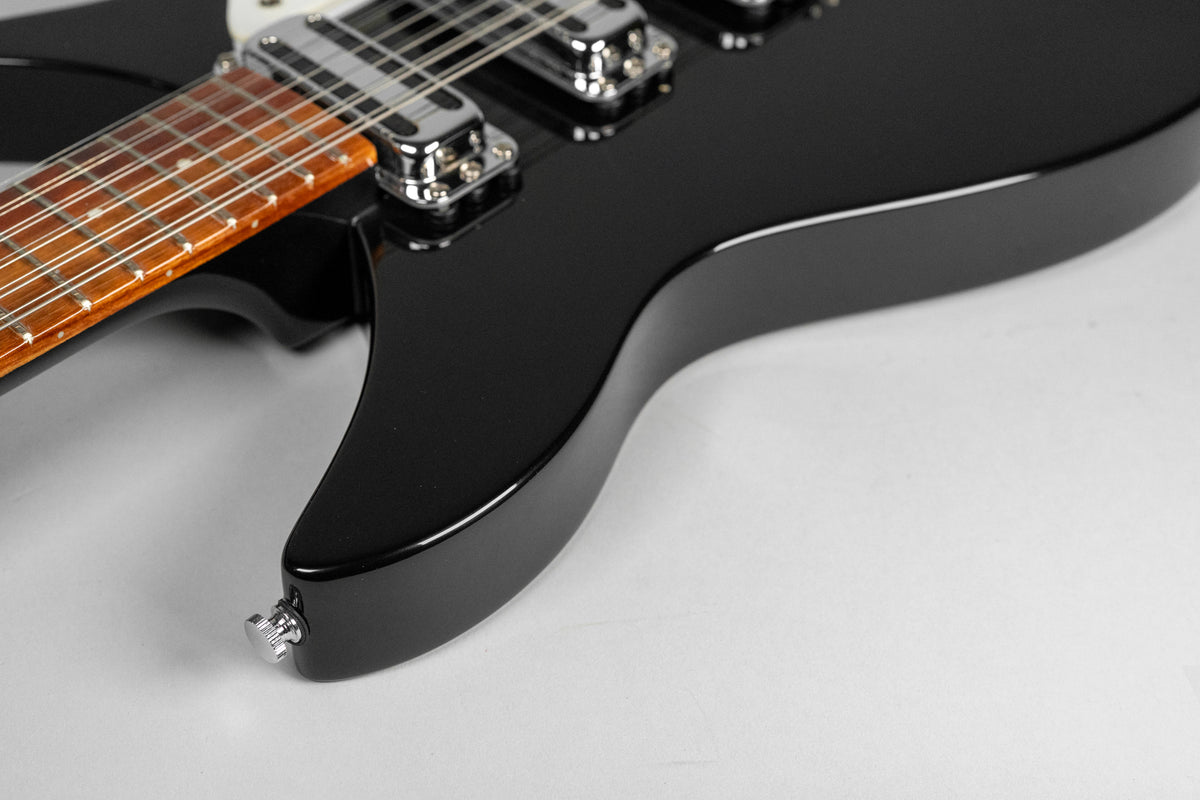 Close-up of the glossy black guitar body, showing the lower horn, output jack, and part of the 12-string neck with chrome pickups.