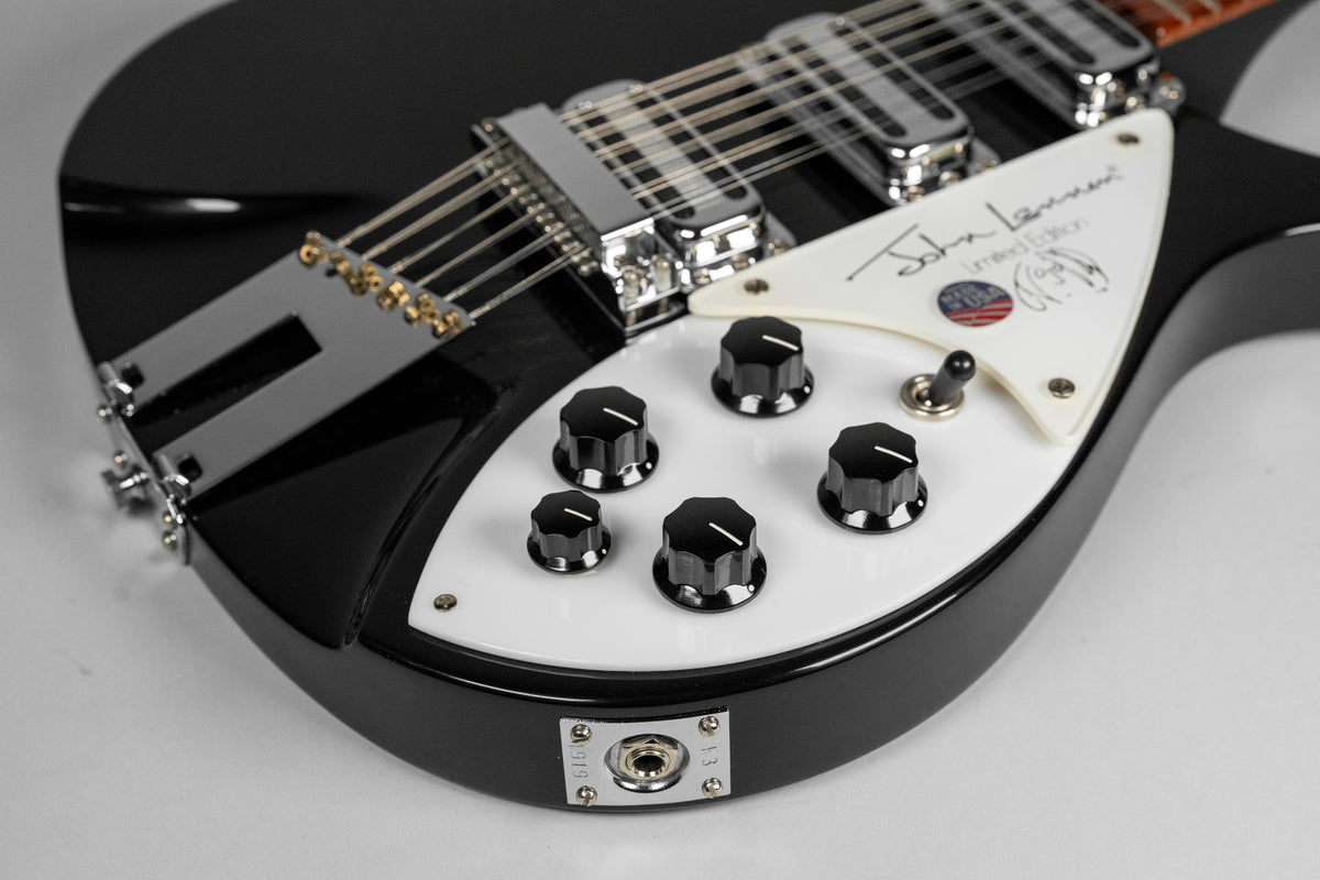 The glossy black body and white pickguard of the 12-string guitar, with six black control knobs and a chrome bridge.