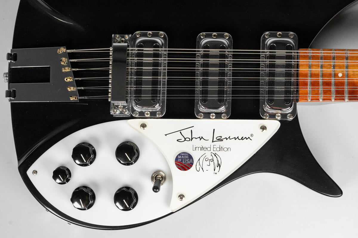 Close-up of the black guitar body, showing the white pickguard with five black control knobs, a toggle switch, and three clear pickups.