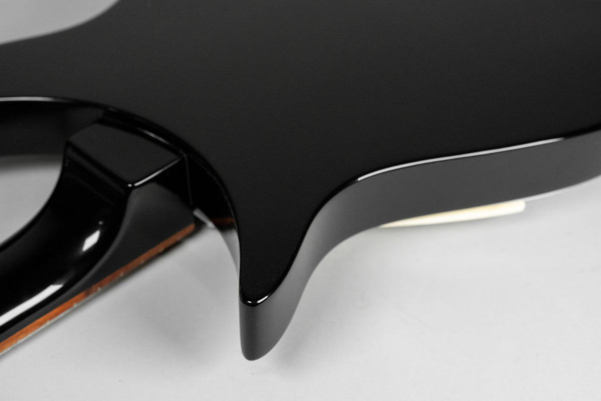 Close-up of the guitar's glossy black body and neck heel, showing a small chip on the neck's binding near the body.