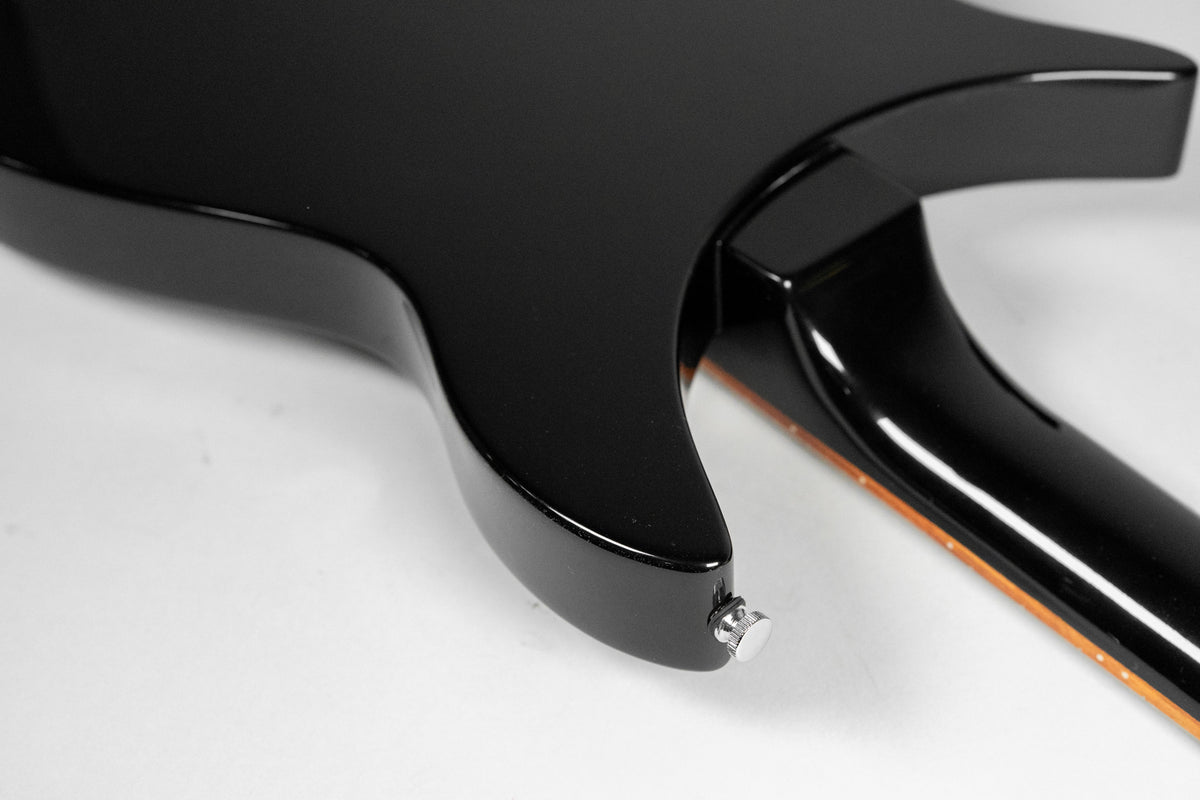 Close-up of the guitar's glossy black body and neck joint, showing the lower strap button and a hint of the neck's binding.