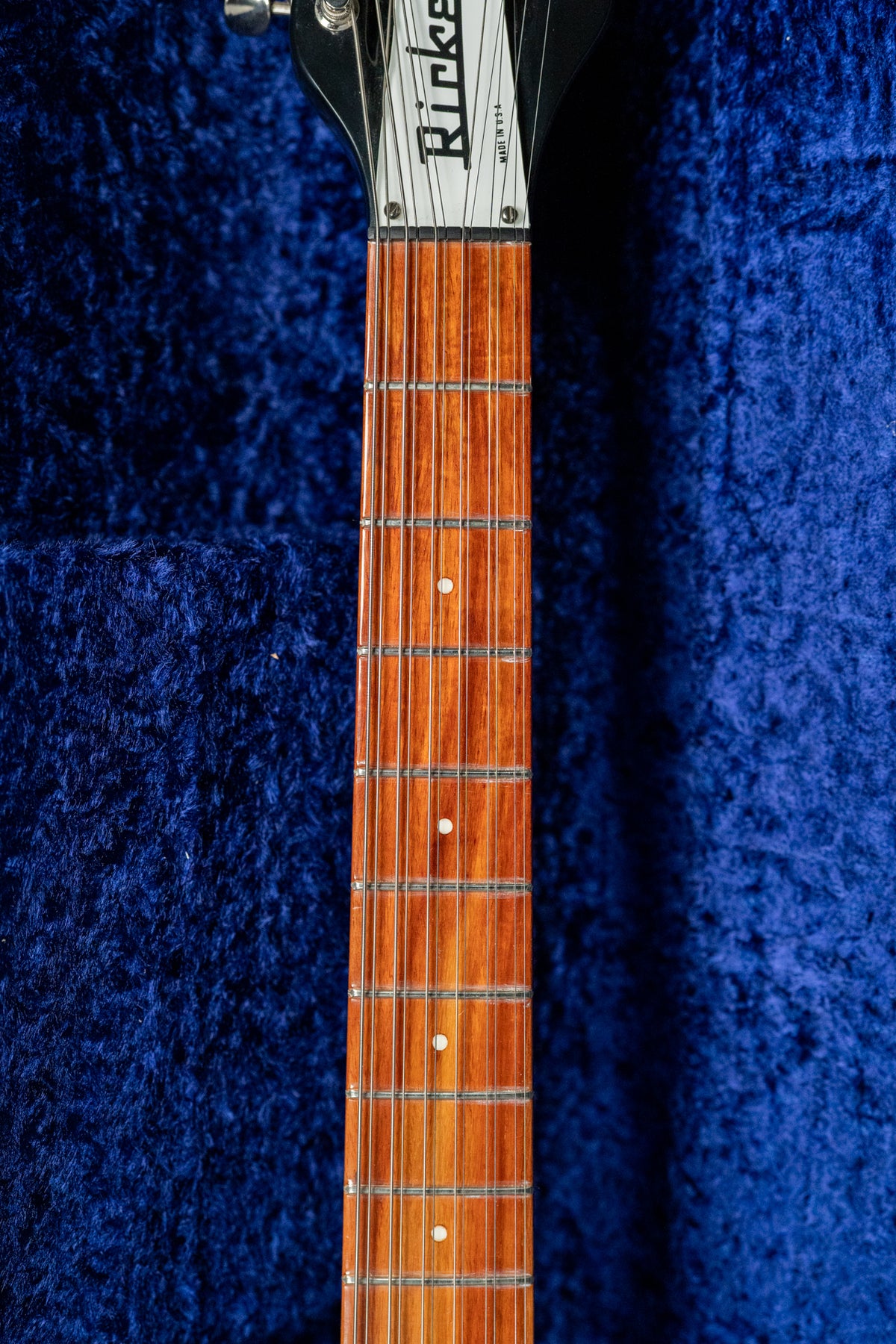 Close-up of the guitar's glossy reddish-brown fretboard with white dot inlays, against a dark blue plush case lining.