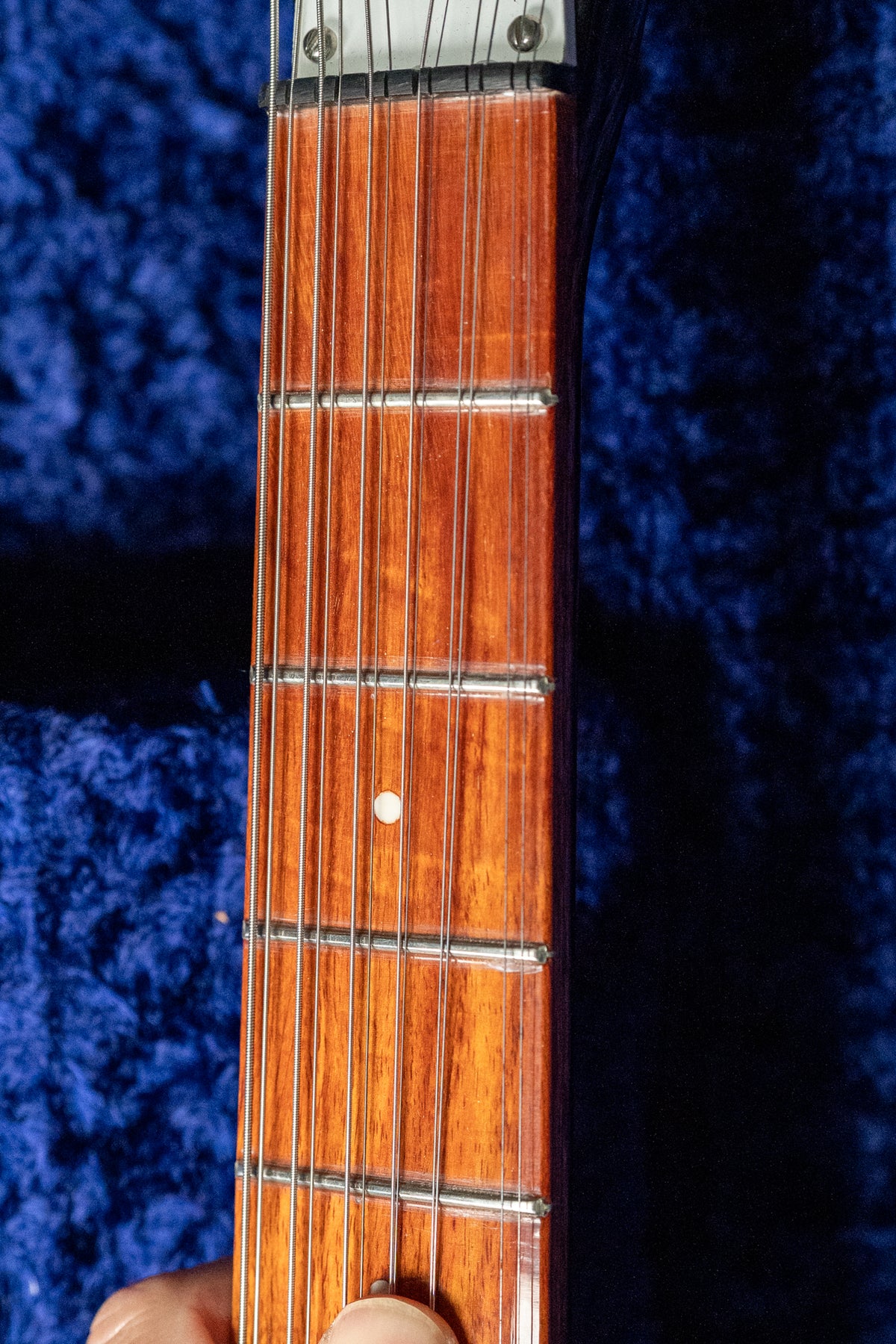 Close-up of the guitar's glossy reddish-brown fretboard with twelve strings, showing a single white dot inlay on the 7th fret.