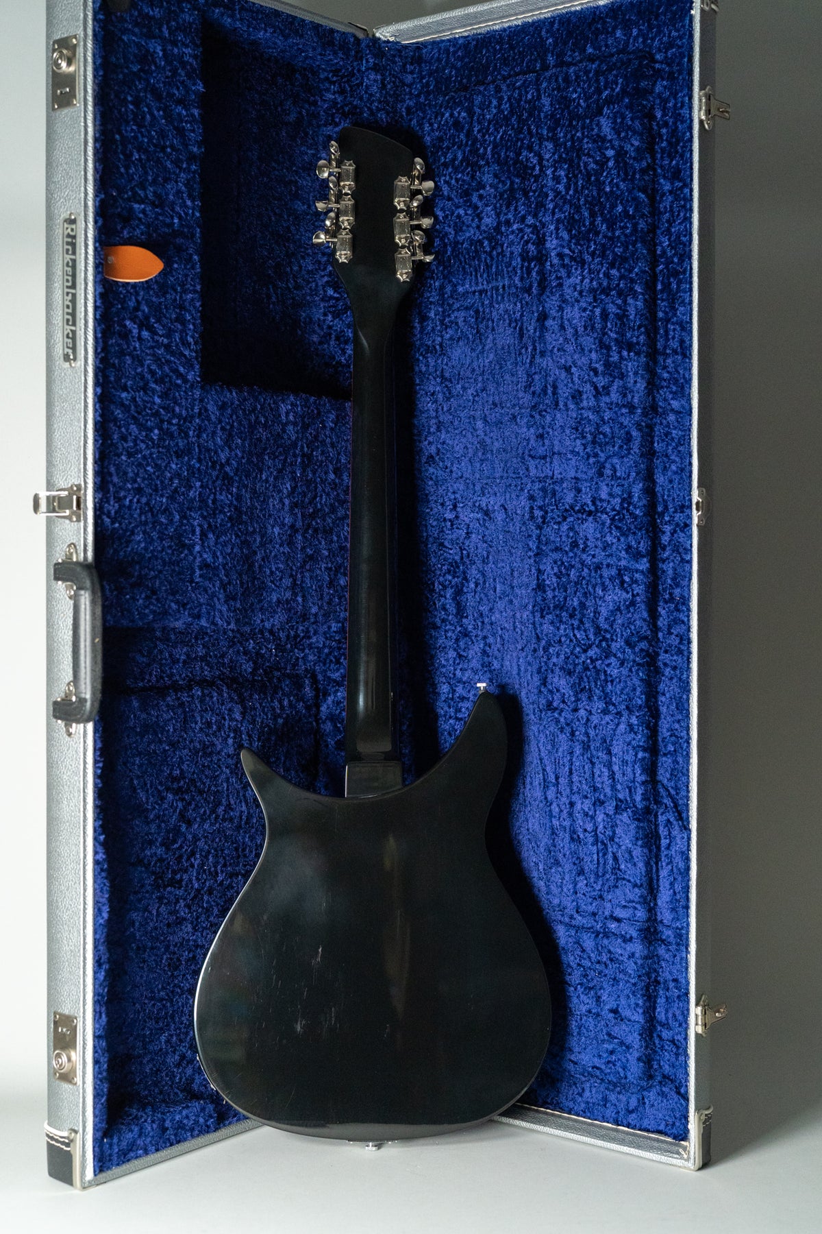 The guitar's glossy black back and neck are visible, with twelve chrome tuners on the headstock, resting in a blue velvet-lined case.
