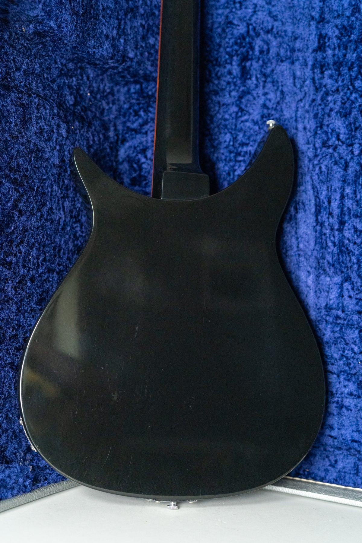 The back of a glossy black guitar body and neck, showing light scratches and a chrome strap button.