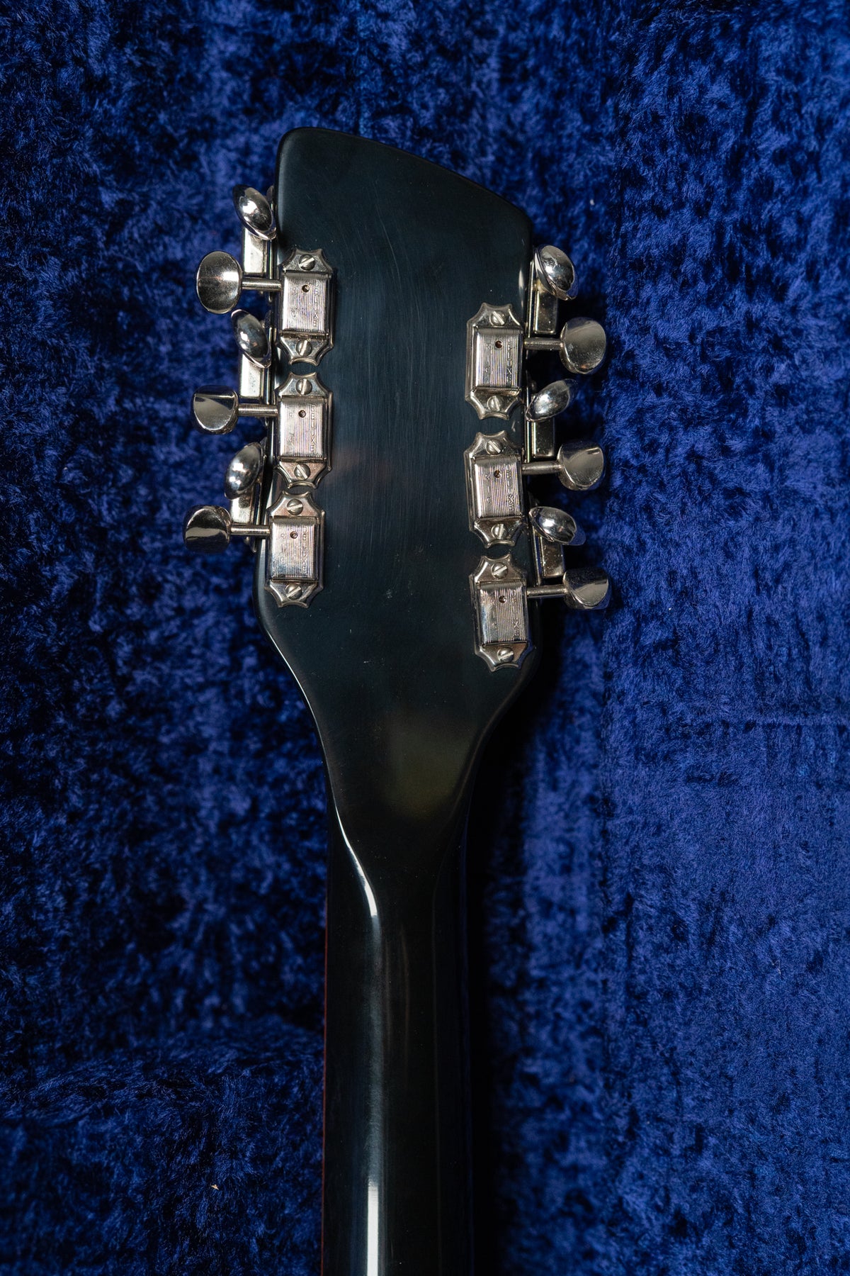 Rear view of the glossy black headstock and upper neck, showing twelve chrome tuners against a blue velvet case lining.