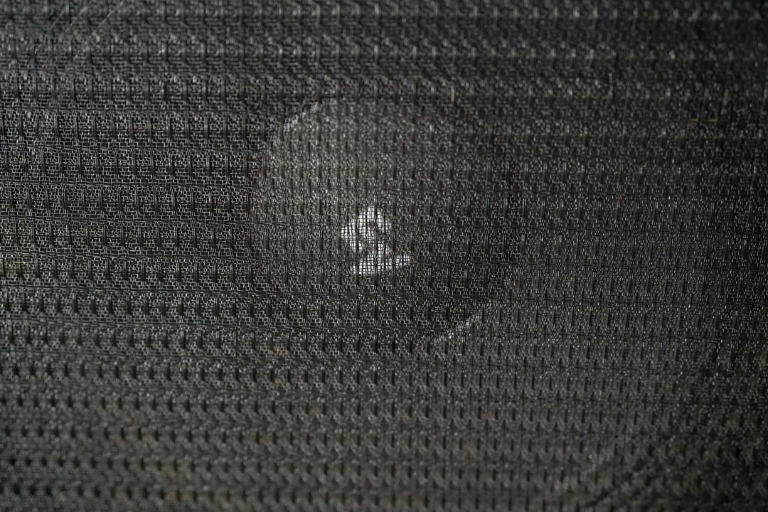 Close-up of the black grille cloth, showing a small tear in the upper center revealing the speaker cone behind.