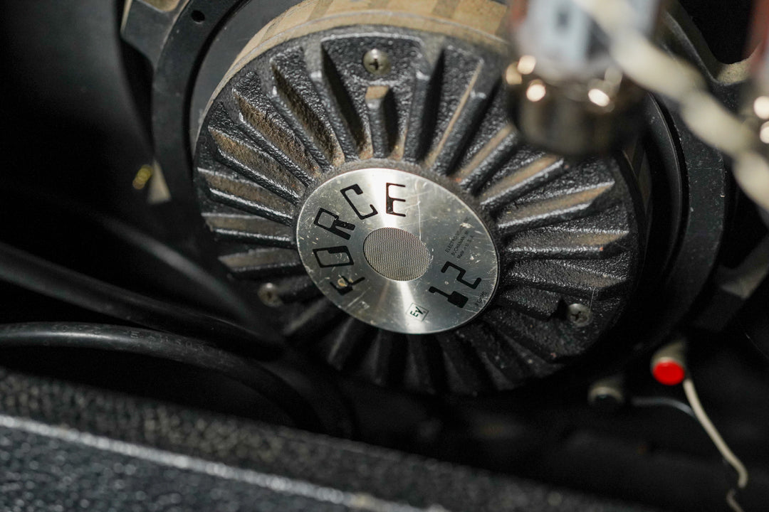 Close-up of the speaker's dusty, ribbed black magnet with a silver cap, showing a vacuum tube and wires in the foreground.