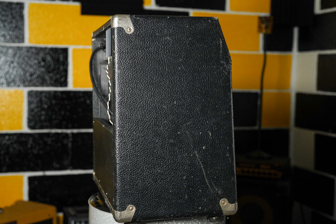 The black textured combo amp is angled to show its right side, revealing scuffs and wear on the tolex and metal corner protectors.